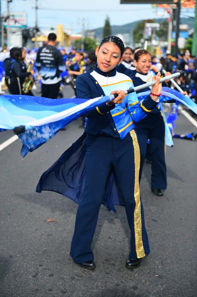 Una joven banderista sonríe mientras manipula horizontalmente el asta de su bandera durante la marcha.