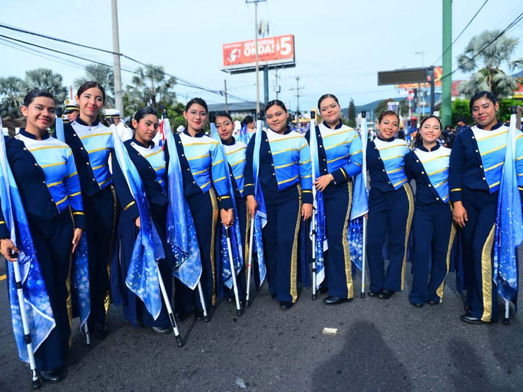 Grupo de jóvenes estudiantes alineadas en la calle posando en uniforme azul y dorado con sus banderas.