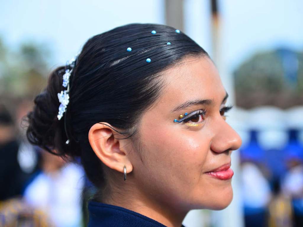 Perfil del rostro y peinado de una estudiante con el cabello recogido en un moño decorado con apliques azules. 