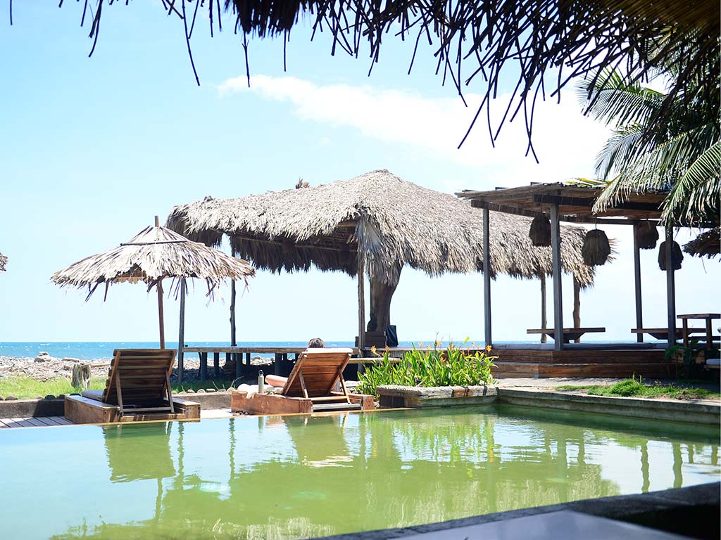 El área de piscina combina una estética tropical con camastros orientados al océano, ofreciendo el refugio perfecto tras una jornada de surf o yoga.