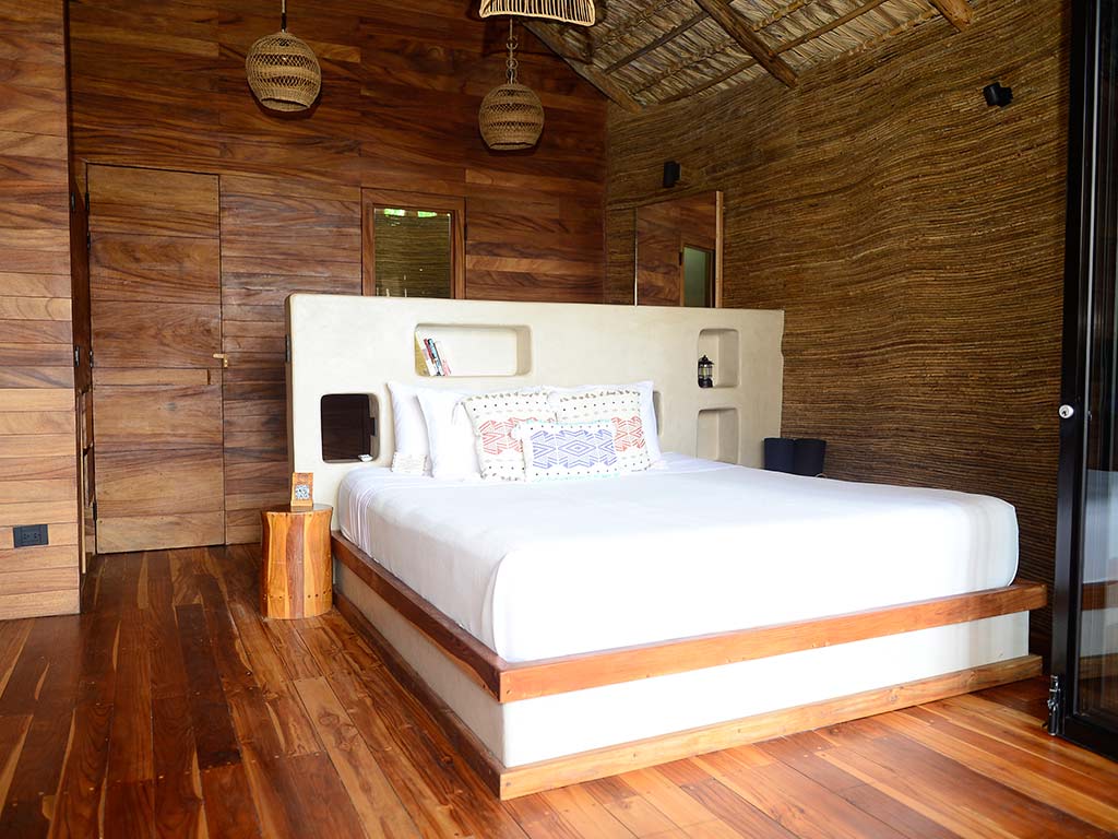 Interior de habitación con cama king, paredes de teca revestidas y decoración artesanal en hotel de playa Mizata.