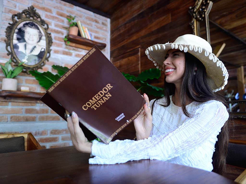 Huésped con sombrero artesanal revisando el menú de Comedor Tunan en Playa Mizata, El Salvador.