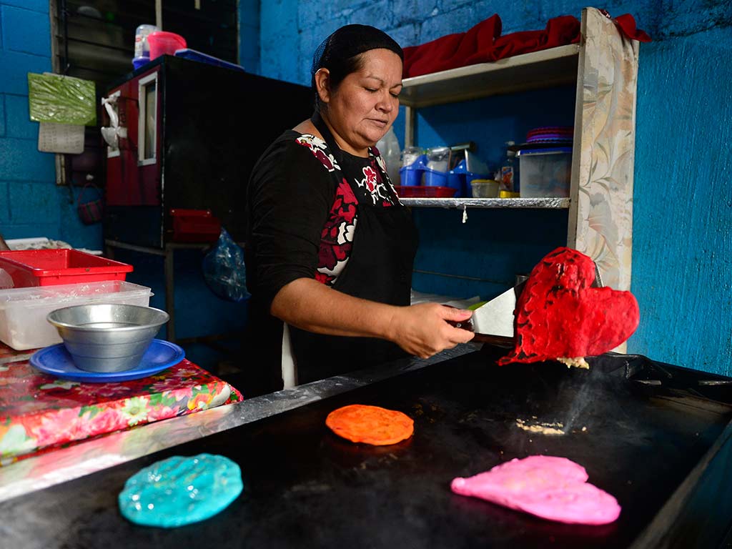 Plancha con pupusas de colores azul, naranja, rosa y roja en forma de corazón.
