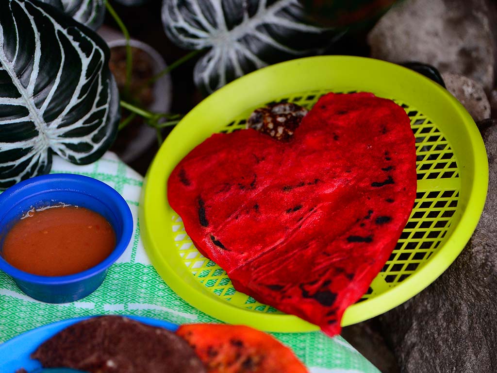 Pupusa salvadoreña roja con forma de corazón servida con salsa en Pupusería Bendición de Dios, Santa Tecla.