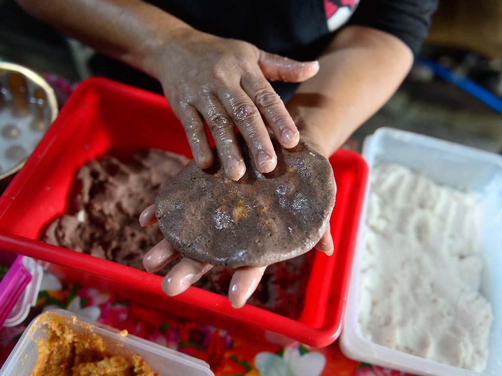 Manos de Marina Quintanilla moldeando una pupusa negrita hecha con masa de frijol en El Salvador.