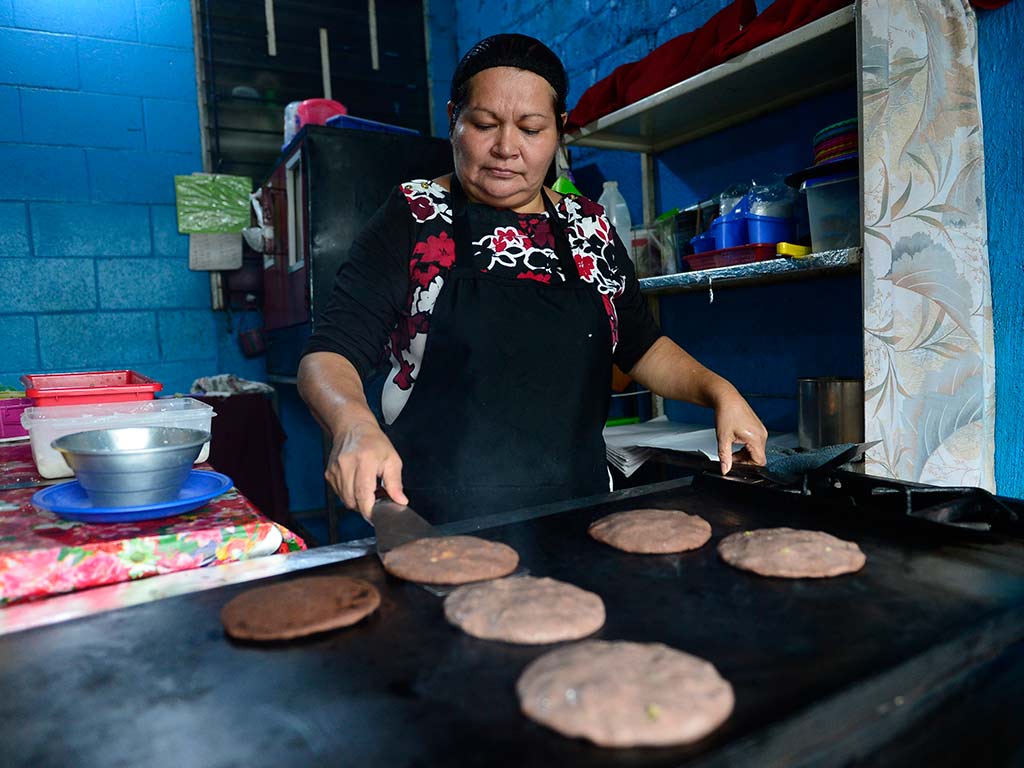 Marina Quintanilla cocinando pupusas de masa de frijol sobre comal caliente en Santa Tecla.