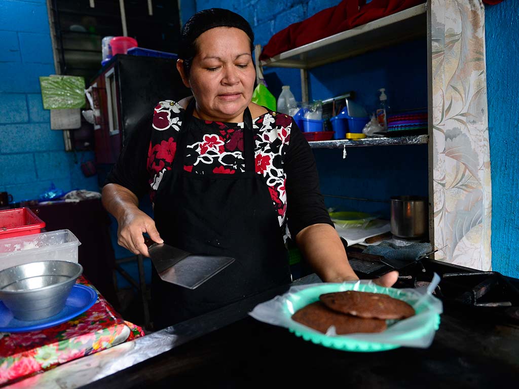 Marina Quintanilla sirviendo pupusas de masa de frijol recién salidad del comal en plato con plástico.