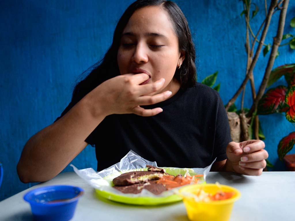 Cliente disfrutando una pupusa negrita de frijol en la colonia Quezaltepeque de Santa Tecla.