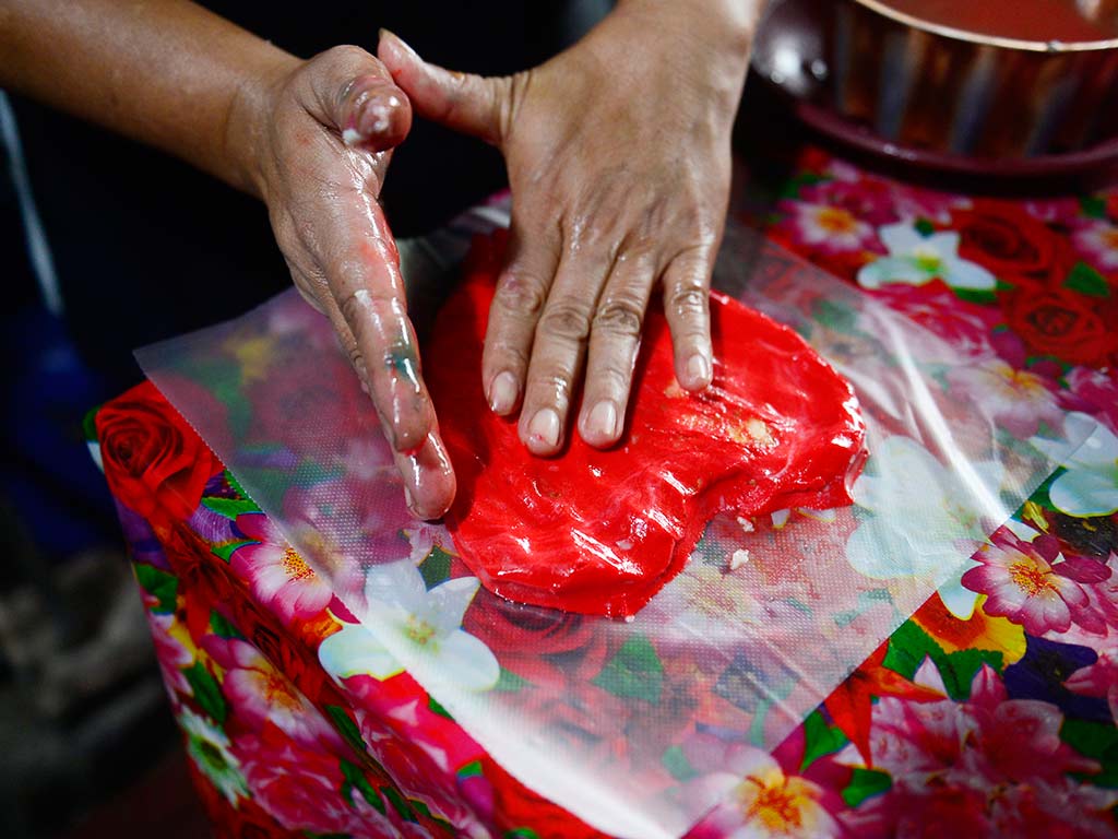 Elaboración artesanal de pupusa roja con forma de corazón sobre mesa de trabajo.