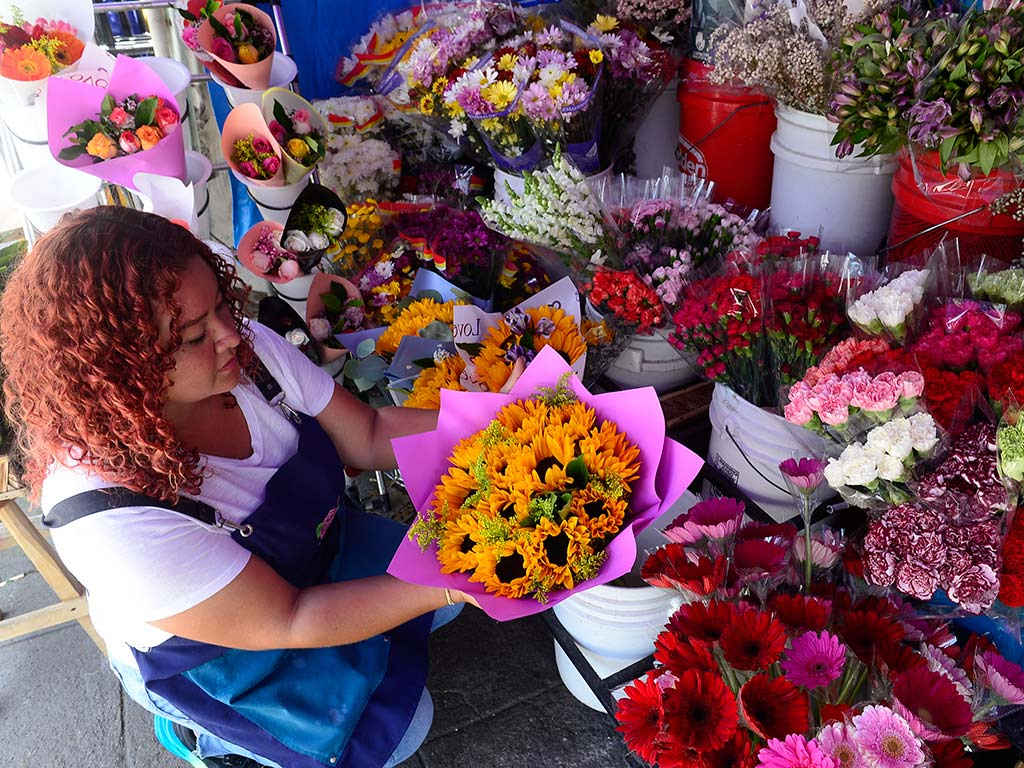 Gabriela Suárez en su floristería frente a Metrocentro mostrando variedad de flores amarillas como rosas y girasoles.
