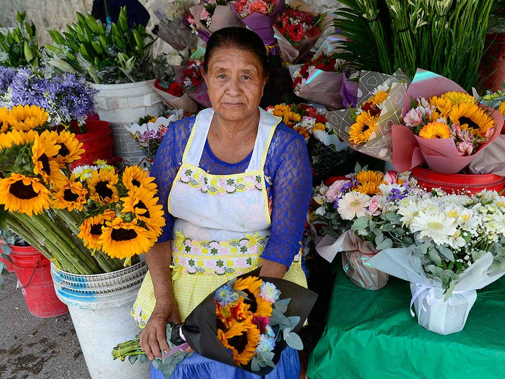María Luz Romero posa junto a un arreglo de flores amarillas en su negocio ubicado en San Benito.