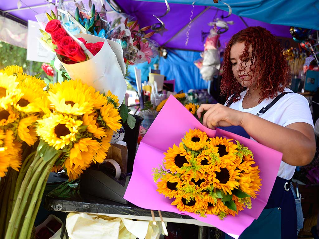 Gabriela Suárez en su floristería frente a Metrocentro mostrando variedad de flores amarillas como rosas y girasoles.