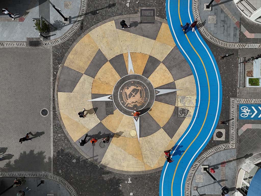 Fotografía aérea cenital amplia del Kilómetro Cero en San Salvador, mostrando la rosa de los vientos en el pavimento y el carril azul para bicicletas.