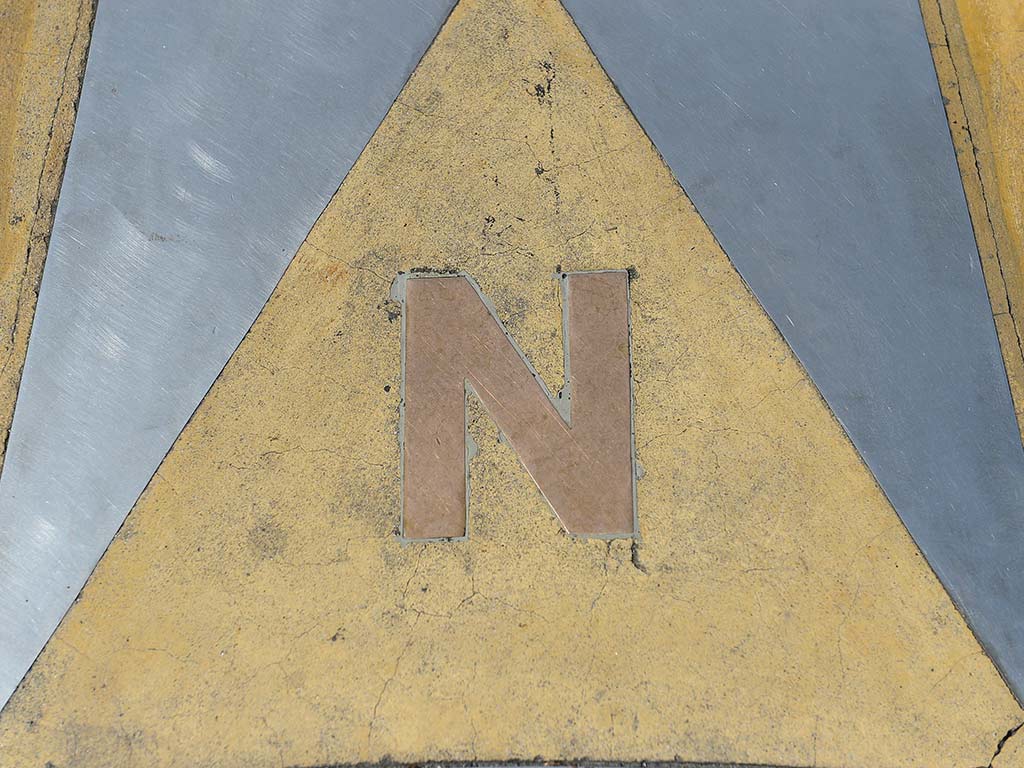 Letra N en dorado sobre un triángulo amarillo señalando el Norte en la rosa de los vientos.
