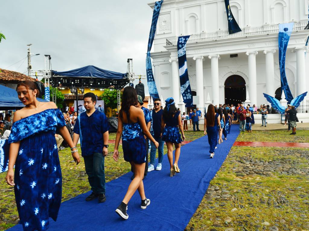 Diseñadores de moda sobre la pasarela junto a modelos que lucen prendas de vestir teñidas en azul añil.