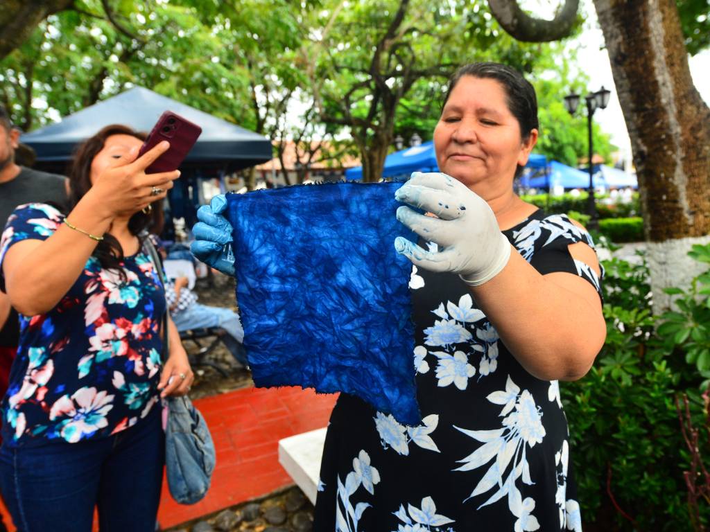 La artesana Rivera exhibiendo una pieza de tela completamente teñida con matices de azul añil.