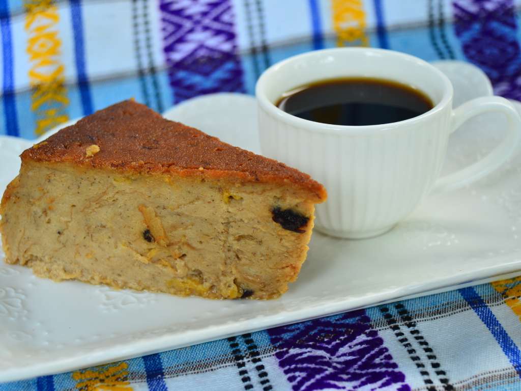 Taza de café caliente acompañada de una porción de budín servida en la mesa.