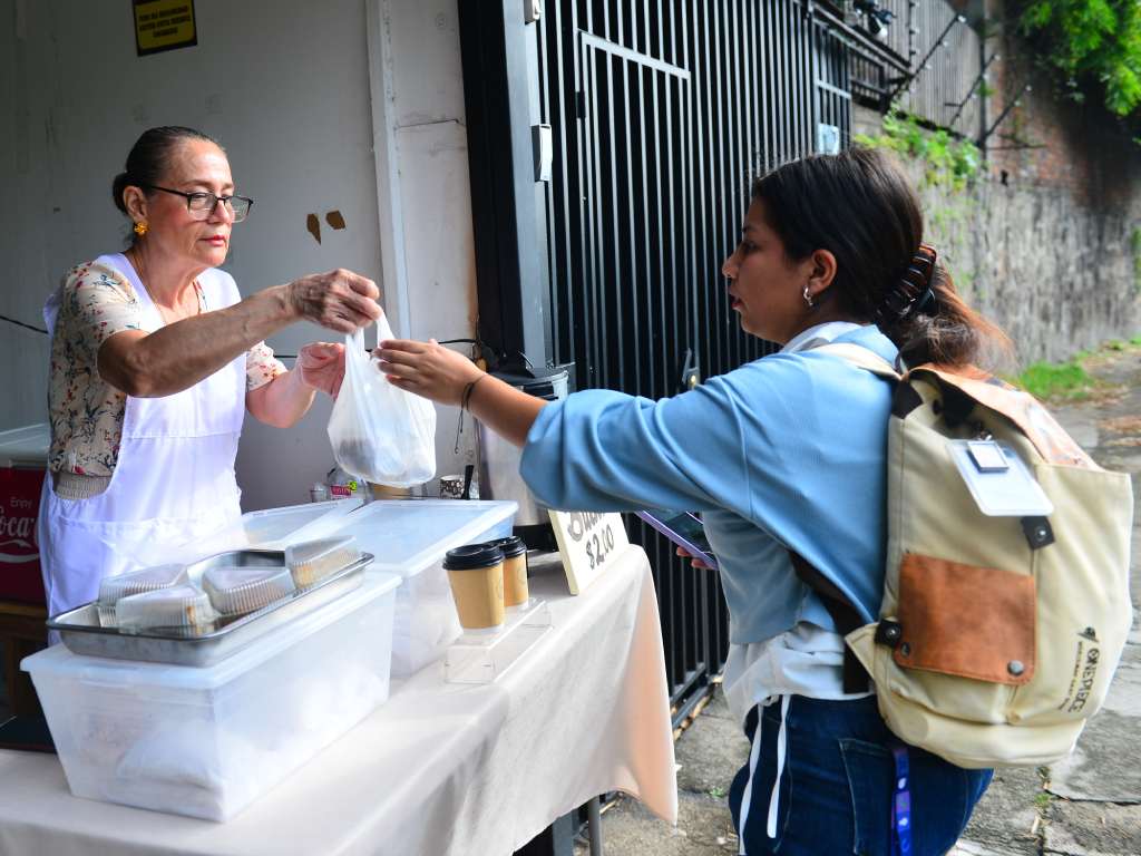 Cliente compra panes variados a un dólar en el puesto de Mamá Tere.