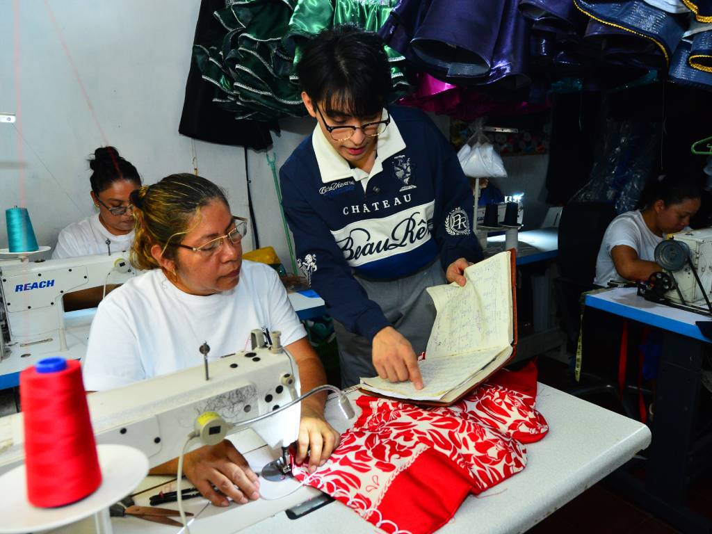 Grupo de personas cosiendo y añadiendo decoraciones detalladas a trajes festivos dentro del taller de confección.