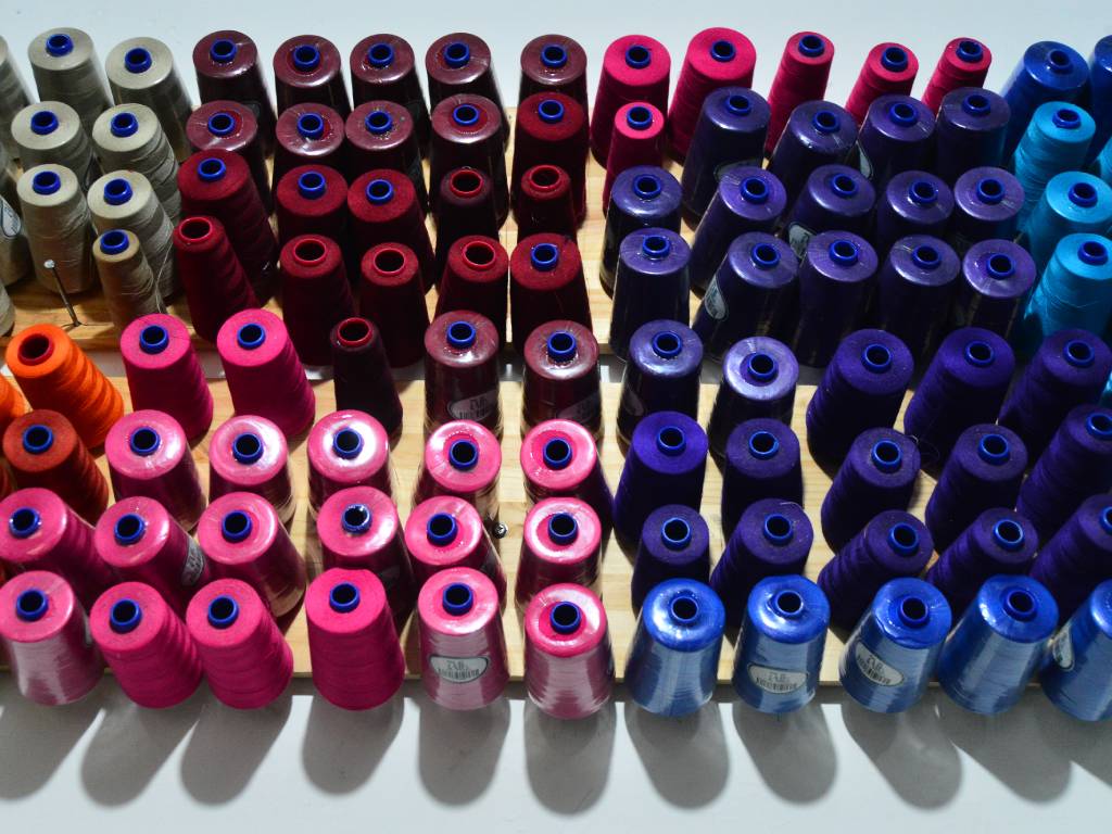 Variedad de carretes de hilo de colores organizados en el taller, listos para confeccionar los trajes de las cachiporras.