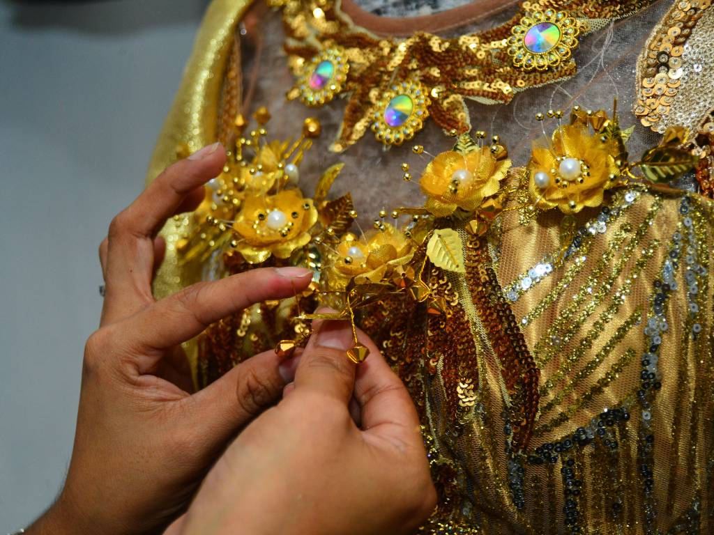Manos sujetando pinzas y pegamento para fijar meticulosamente pequeños accesorios sobre el diseño del vestuario.