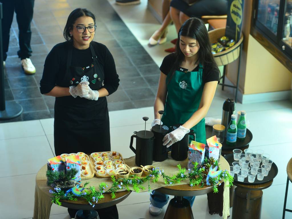 Un barista realiza una demostración en vivo mostrando granos de café y tazas preparadas ante los asistentes.