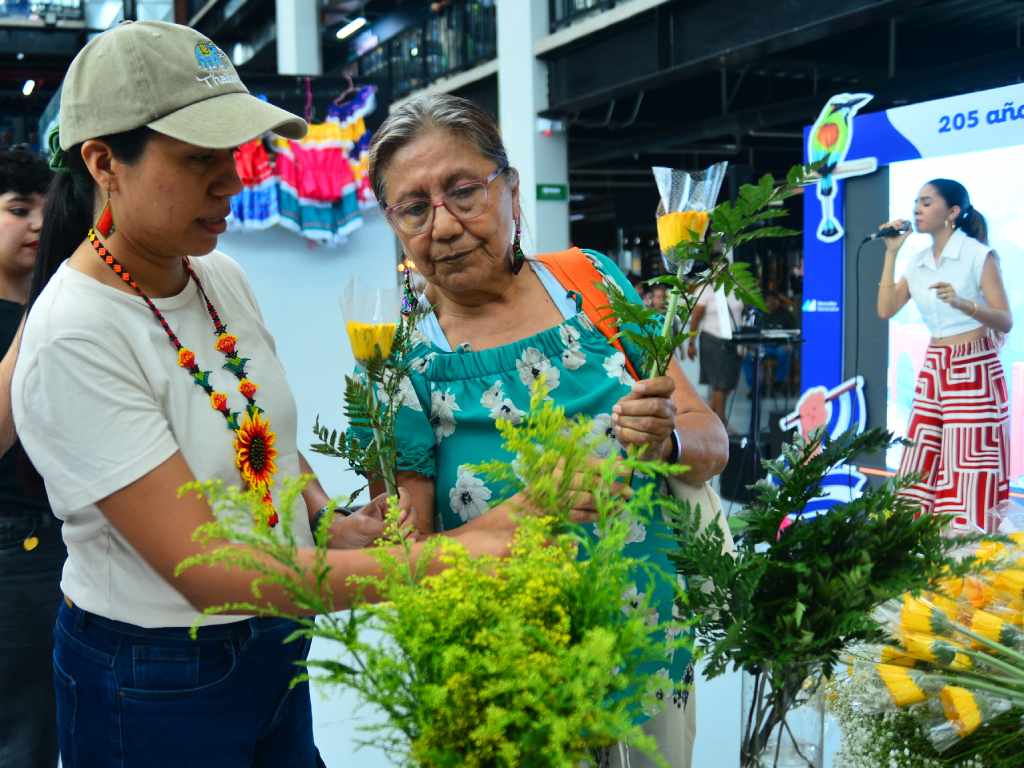 Personas comprando arreglos de flores amarillas en los puestos de un mercado para regalar el 21 de septiembre.