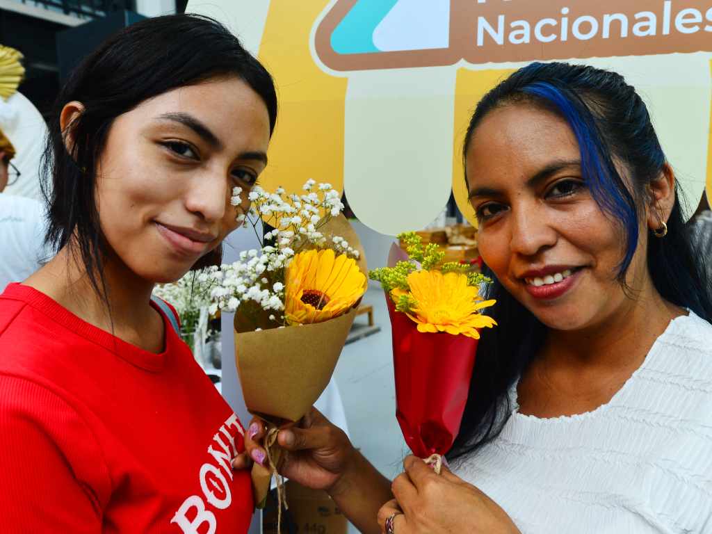 Madre e hija sonríen mientras sostienen y muestran sus arreglos florales amarillos durante el evento.