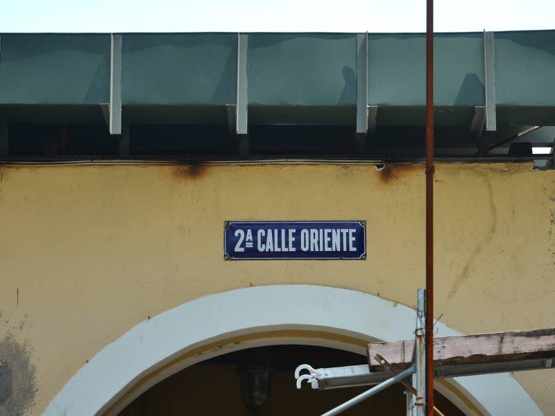 Primer plano de un rótulo de calle azul que dice "2A CALLE ORIENTE" fijado sobre una sección de madera de la estructura de construcción del Portal Sagrera.