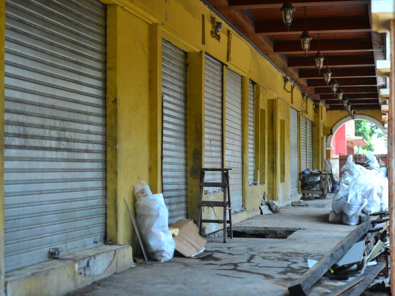 Vista del pasillo interior del Portal Sagrera en construcción, con el suelo de cemento picado y materiales de construcción como sacos de cemento y madera apilados frente a persianas metálicas cerradas.