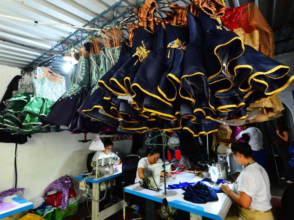 Grupo de trabajadoras cosiendo trajes festivos en las máquinas de escribir del taller junto a Roni y su madre.