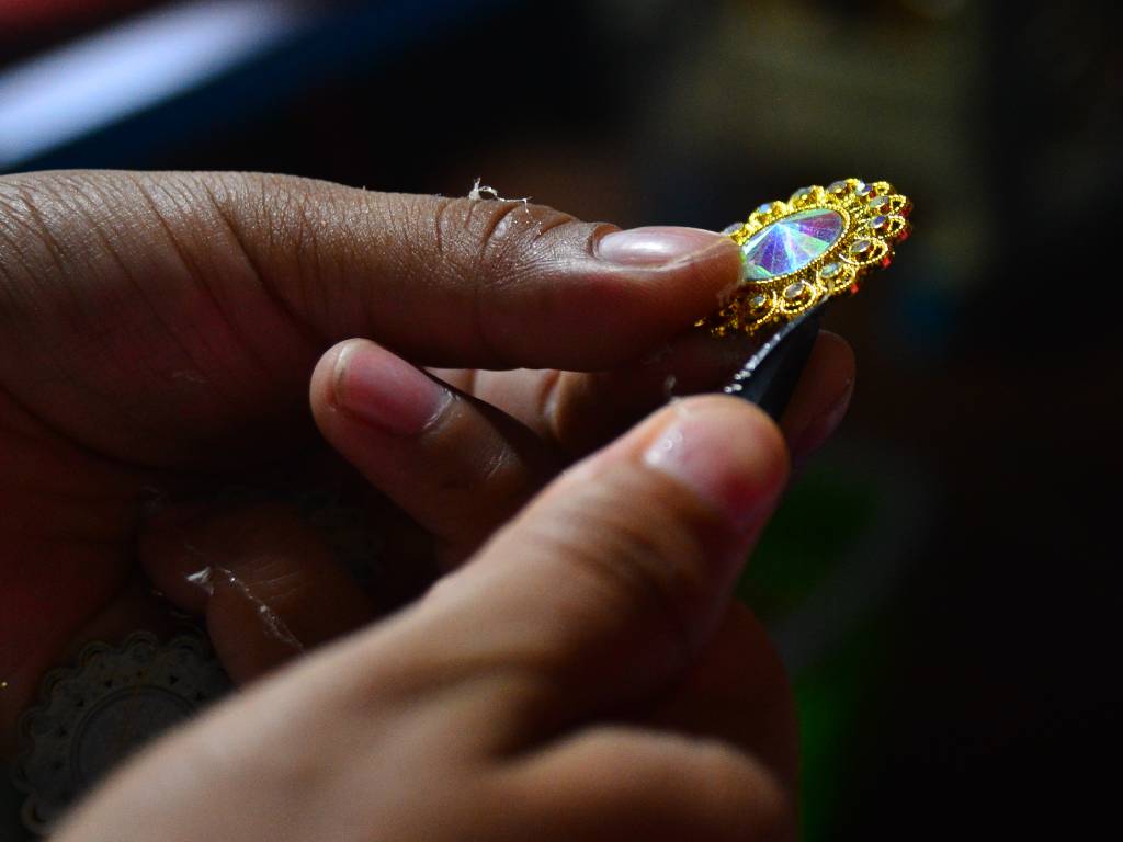 Detalle en primer plano de manos artesanas aplicando delicadamente accesorios sobre el diseño del traje de cachiporra.