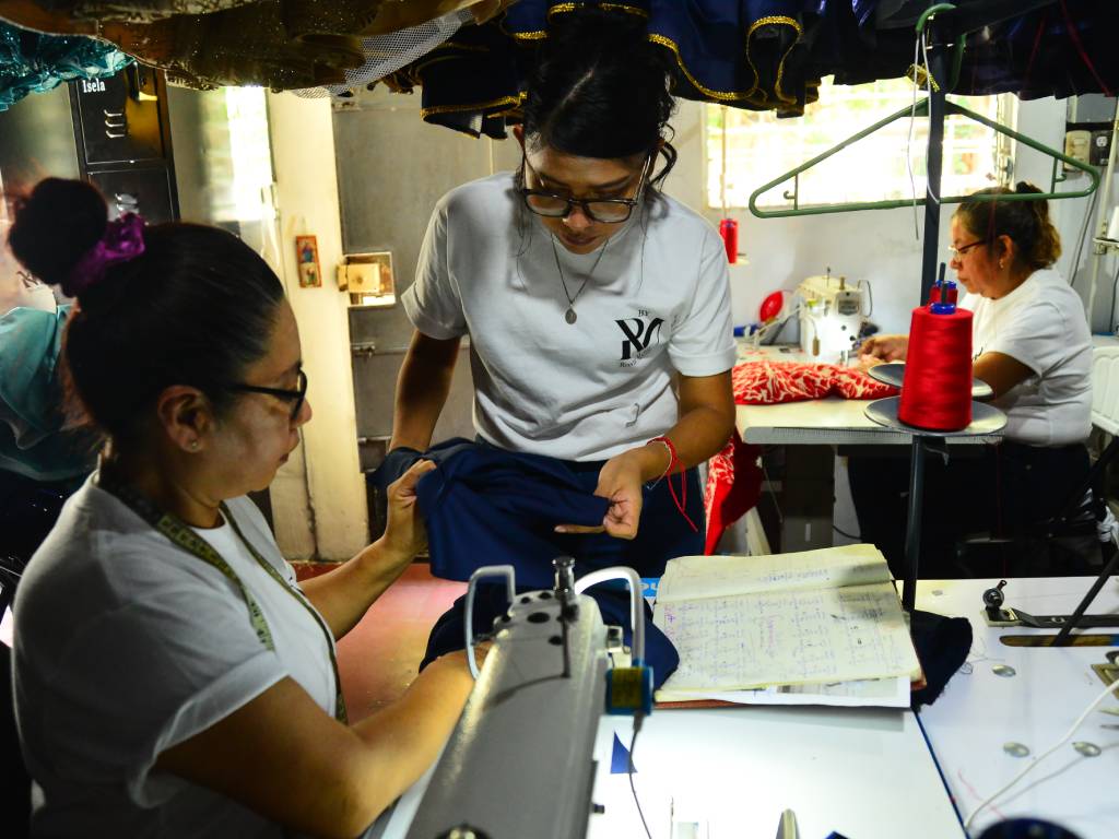Dos colaboradoras del taller trabajando juntas y ayudándose a sostener la tela mientras realizan acabados a mano.
