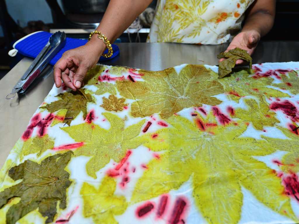 Manos de la diseñadora retirando la hoja de higuero para revelar el patrón botánico impreso sobre el textil.