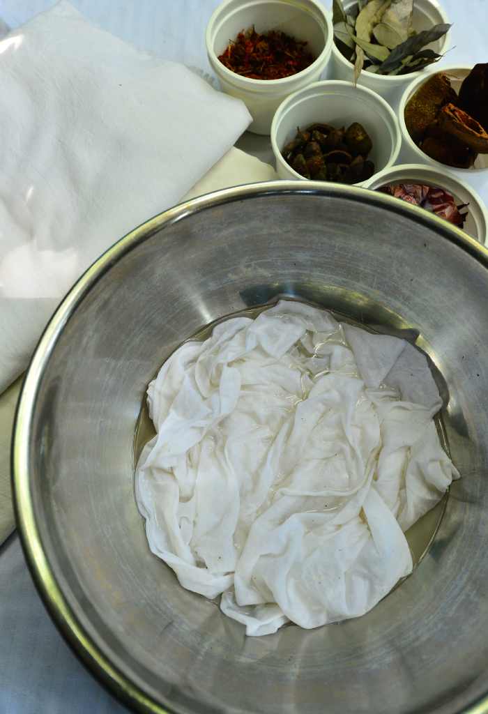 En el recipiente se puede observar tela humedecida con agua de alumbre, a la izquierda se encuentra lienzo de algodón y en los recipientes pequeños materia prima vegetal para estampar las telas.