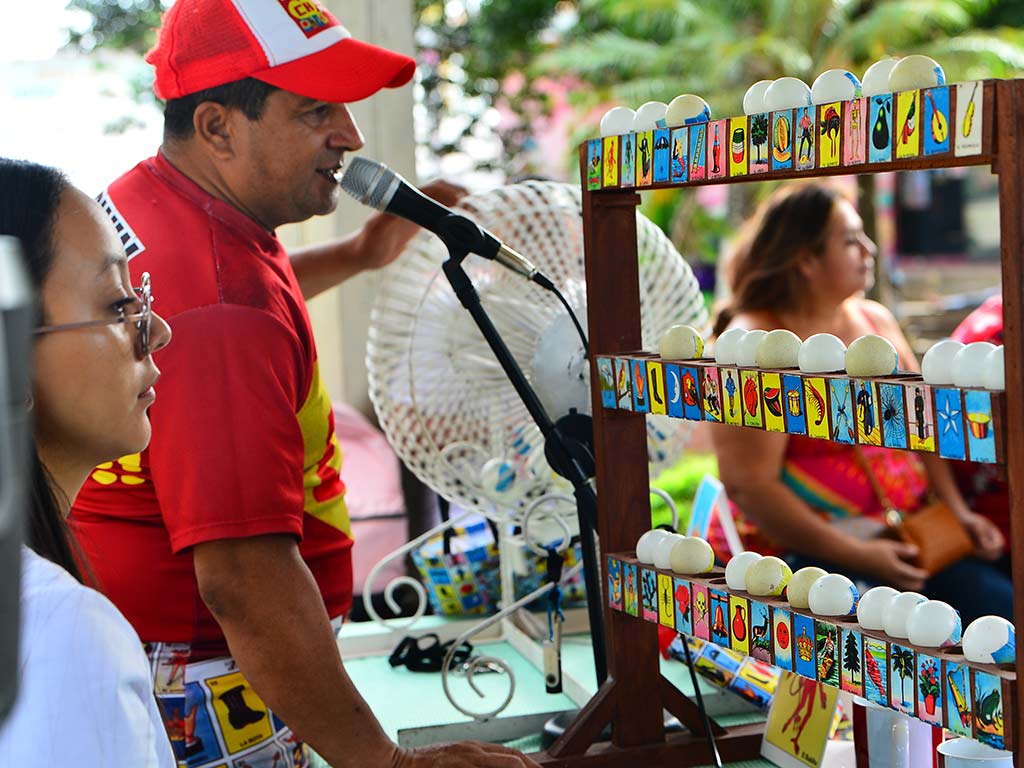 Hombre con gorra roja cantando las cartas en un micrófono junto al estante de madera con las esferas.