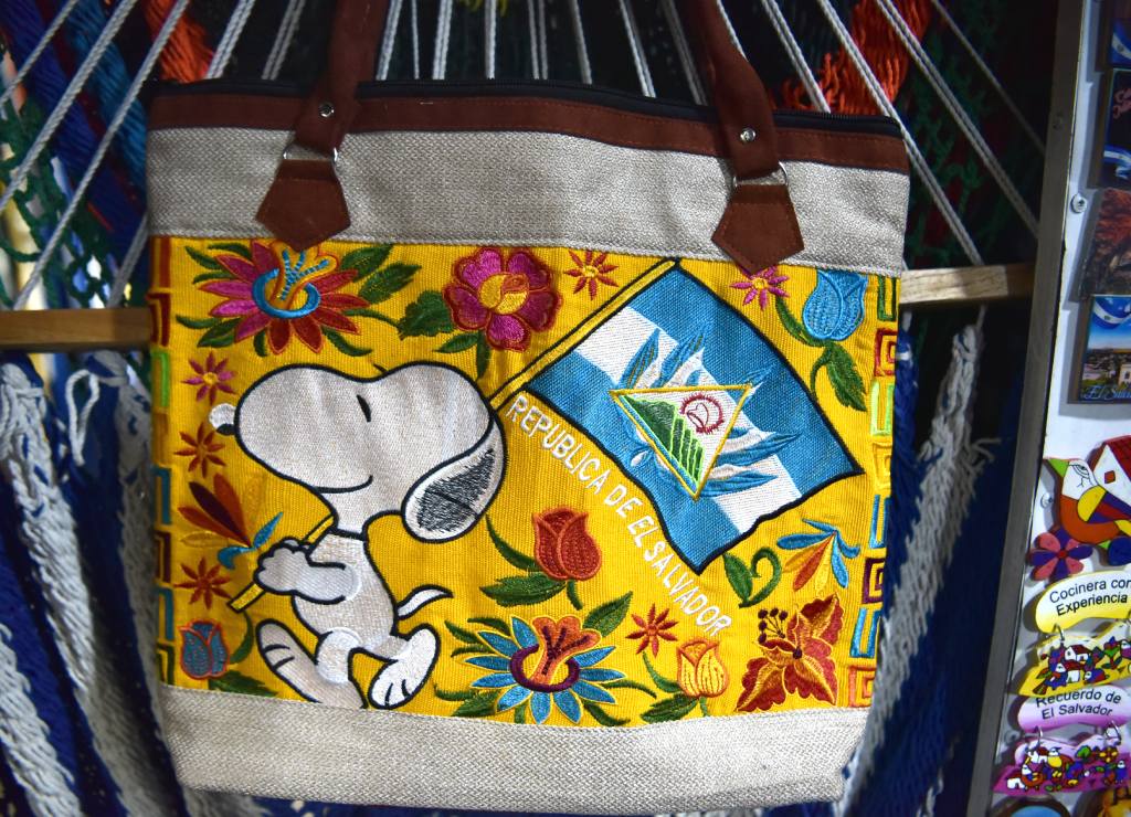 Bolso artesanal de tela amarilla con bordados florales, la bandera nacional y Snoopy.