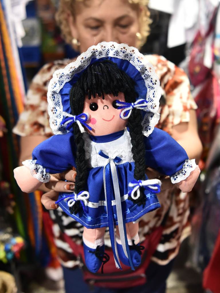 Una mujer sostiene una muñeca con vestido azul y blanco y encajes.