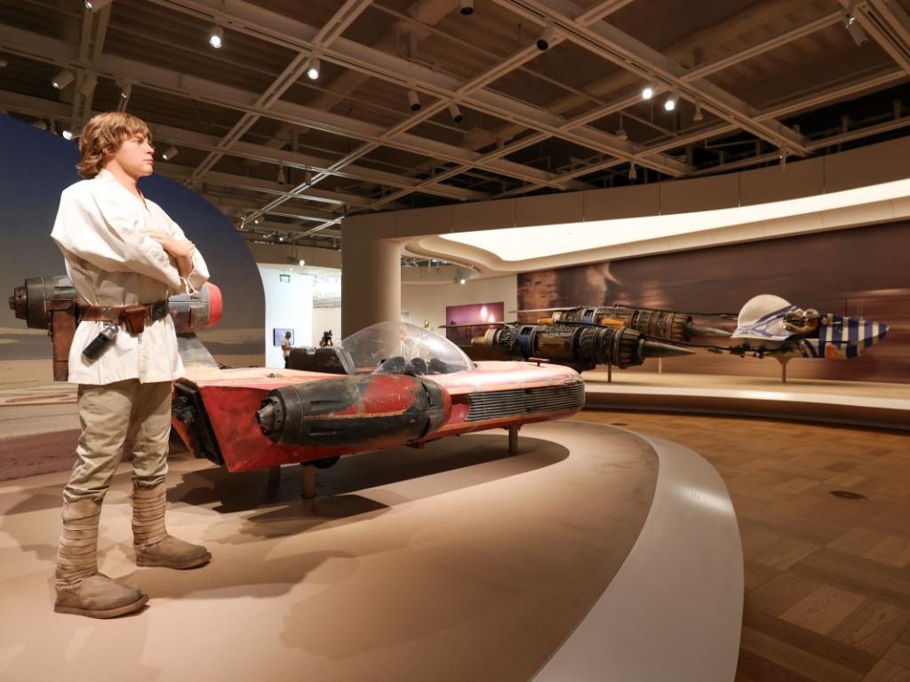 Estatua a tamaño real de Luke Skywalker junto a su icónico landspeeder rojo en una sala de exposición del Museo Lucas.