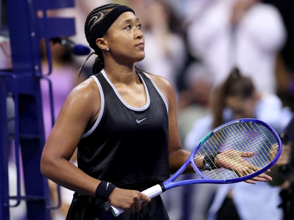 Naomi Osaka saluda al público tras vencer a Anastasia Zakharova en la primera ronda del US Open 2026, luciendo su conjunto negro de Nike.