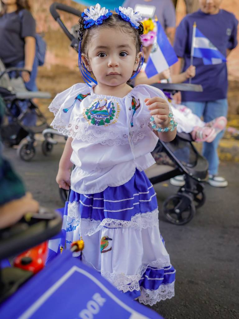 diante posa en la calle vistiendo un traje alegórico con los tonos azul y blanco de la bandera salvadoreña.
