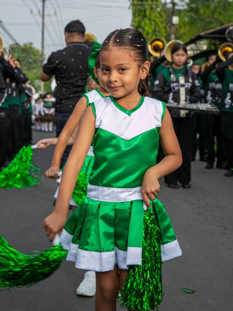 Una porrista sostiene pompones de colores a juego con su uniforme durante una presentación en la calle.