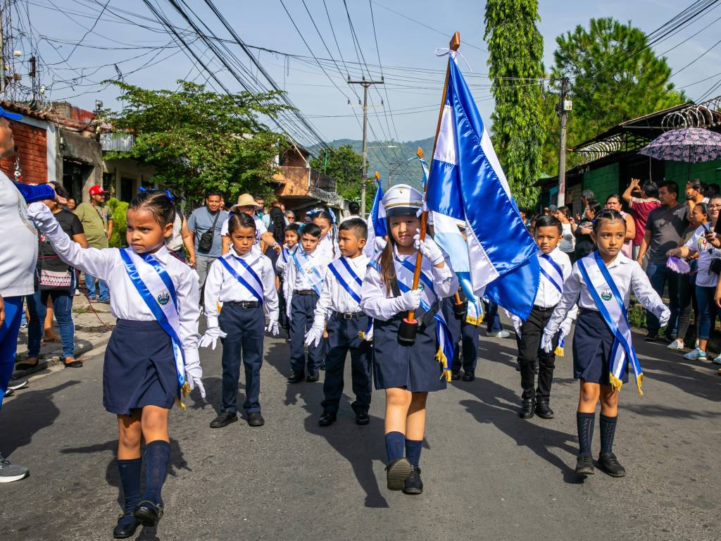 Representantes de distintas instituciones locales marchan organizadamente por una calle durante un desfile cívico.