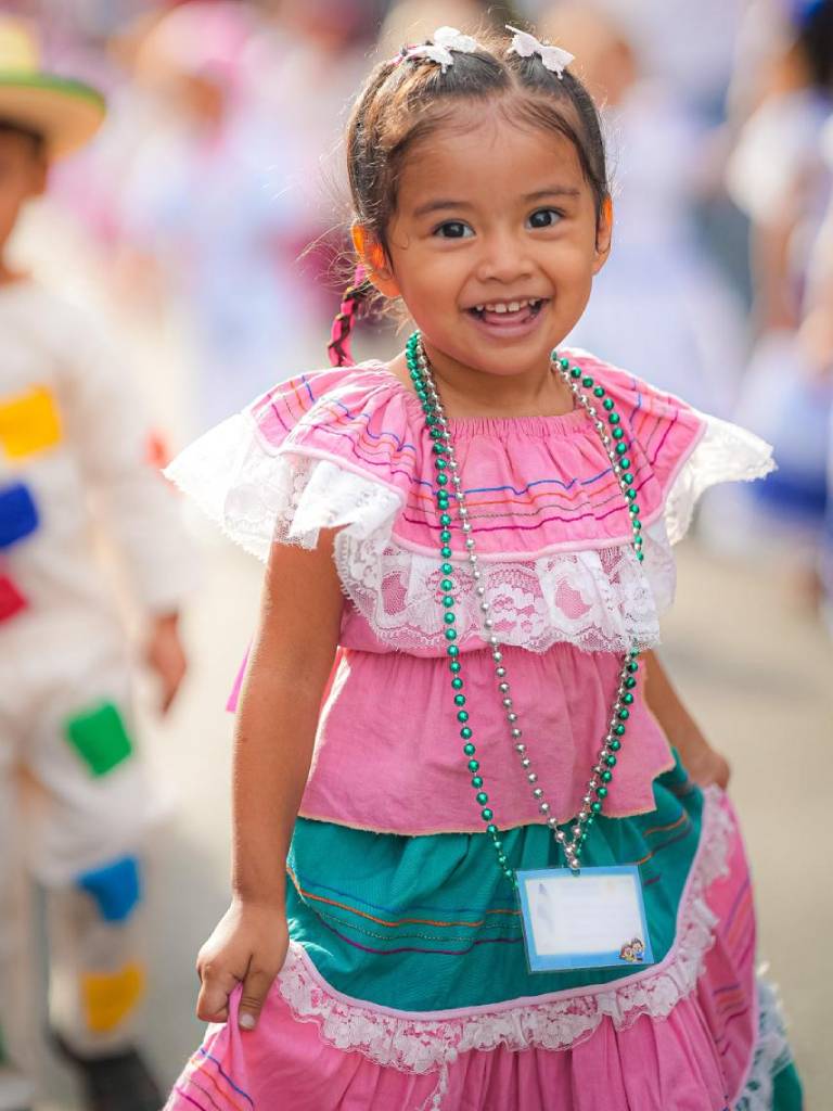 Grupo de participantes luciendo trajes folclóricos tradicionales de vistosos colores marchan durante una presentación cultural.