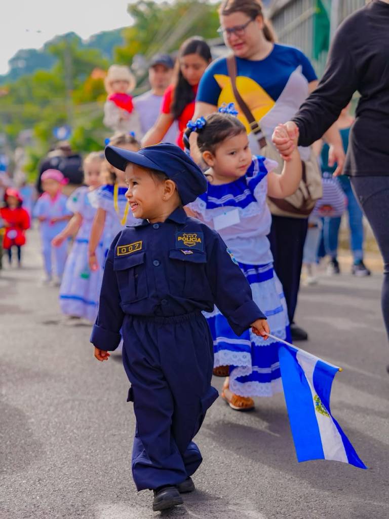 Niña vestida con el uniforme completo de agente de policía sonríe y posa durante un desfile infantil.