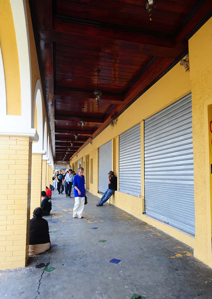 Fotografía histórica que muestra la vida comercial y peatonal bajo los arcos del Portal Sagrera, con personas vestidas de la época y letreros de tiendas antiguos.