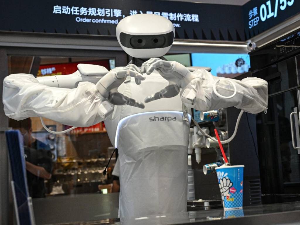 El robot humanoide Sharpa junta sus manos de cinco dedos formando el gesto de un corazón frente a una clienta en la barra de la heladería Dairy Queen.
