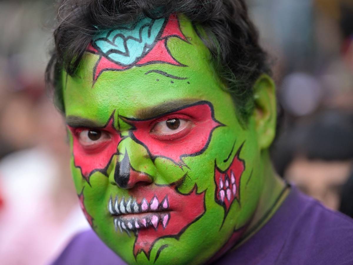 Acercamiento a un asistente caracterizado con maquillaje facial estilo cómic en tonos verde, rojo y negro.