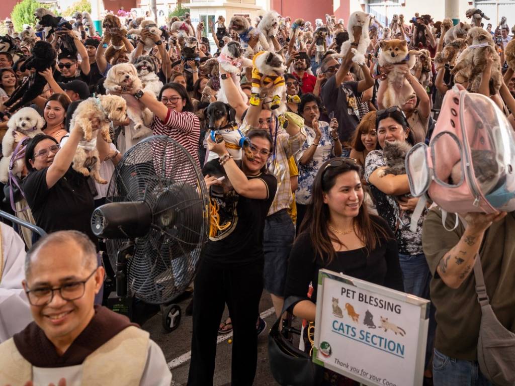 Devotos de distintas edades sosteniendo sus mascotas frente a un templo en una jornada masiva de bendición.