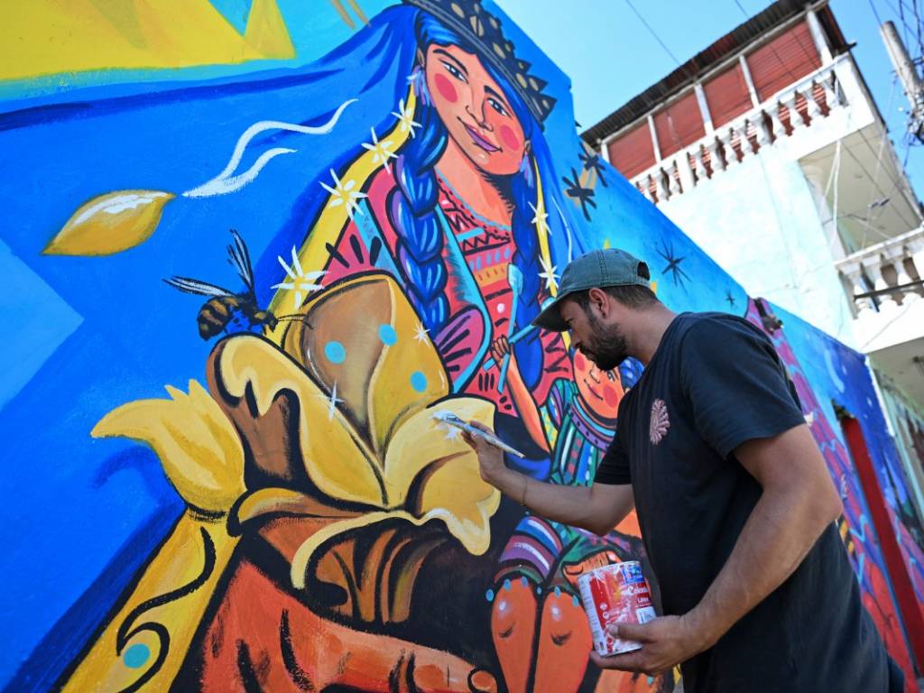 El artista Luis Fernando Izquierdo pintando con pincel sobre un mural de la Virgen María y el niño Jesús en una pared.